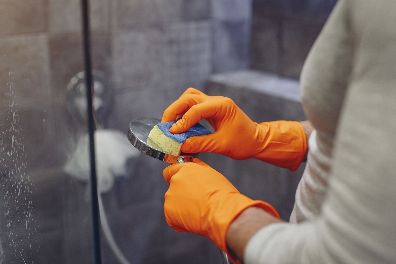 Crop faceless male in orange rubber gloves wiping by sponge shower nozzle